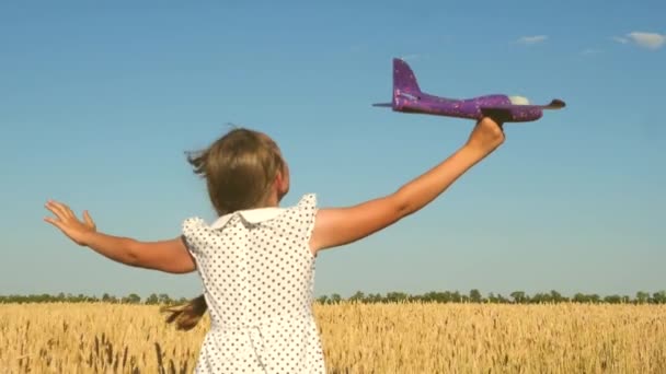 Gelukkig meisje rent met een speelgoedvliegtuigje op een veld bij zonsondergang. kinderen spelen speelgoed vliegtuig. tiener droomt van vliegen en piloot worden. Het meisje wil piloot en astronaut worden. Langzame beweging - Video