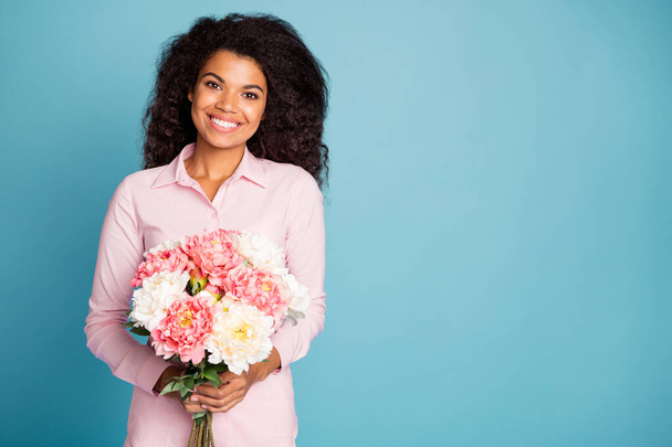 Photo of pretty wavy dark skin lady holding big fresh flowers bunch enjoy unexpected surprise 8 march morning wear pink shirt isolated blue color background - Φωτογραφία, εικόνα