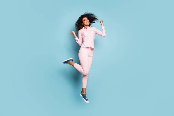 Full length photo of amazing dark skin lady jumping high celebrating cool victory triumphing wear pink shirt trousers sneakers isolated blue color background - Foto, immagini