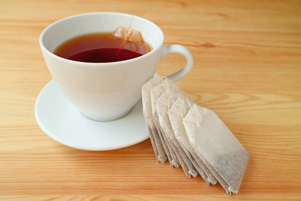 Kopje warme thee met theezakjes geserveerd op houten tafel - Foto, afbeelding