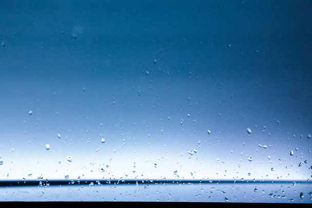 Νερό πέφτει στο παράθυρο, από την εστίαση στην προβολή λιμάνι και μπλε φόντο του ουρανού. - Φωτογραφία, εικόνα