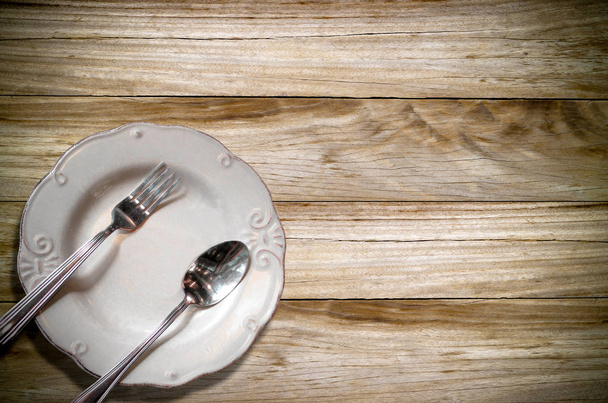 Gros plan d'un plat en céramique vide avec cuillère et fourchette brillantes sur la planche en bois, concept de nourriture et de boisson pour le fond
. - Photo, image