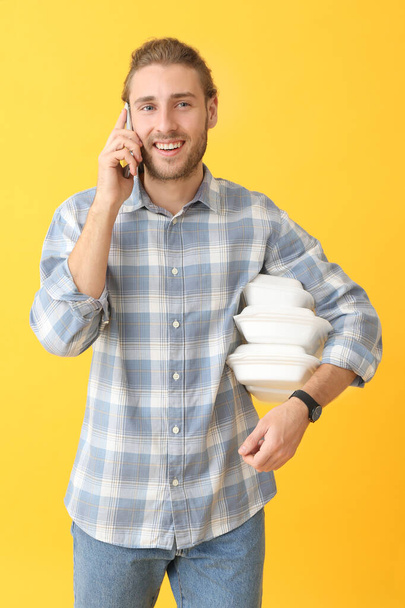 Portrait d'homme heureux avec des conteneurs de nourriture parlant par téléphone mobile sur fond de couleur
 - Photo, image
