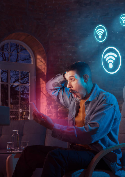 Man using gadget and receive neon notifications at home at night - Fotó, kép