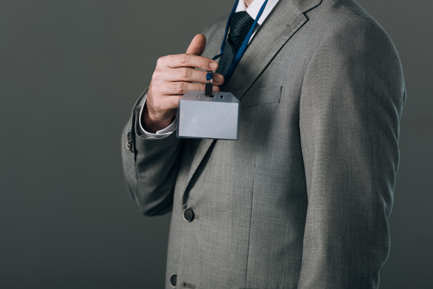 Cropped view of man in suit holding badge isolated on grey - Photo, Image