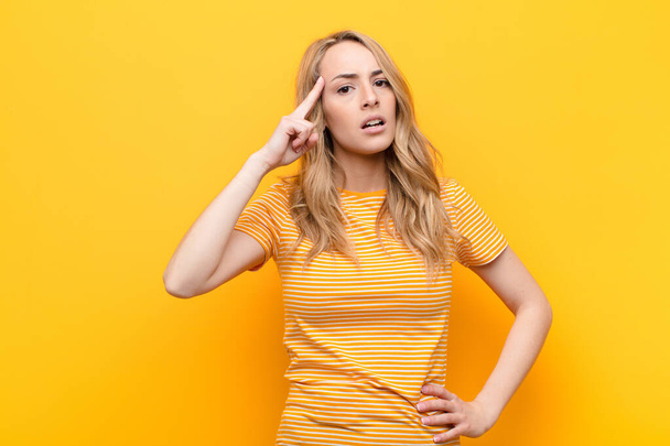 young pretty blonde woman looking surprised, open-mouthed, shocked, realizing a new thought, idea or concept against flat color wall - Photo, image