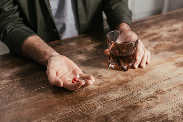 Cropped view of man holding whiskey glass and pills in hands - Фото, изображение