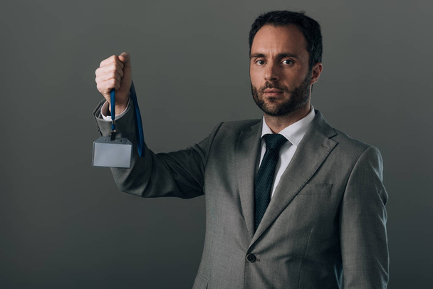 Mann im Anzug hält Abzeichen mit Kopierraum isoliert auf grau - Foto, Bild