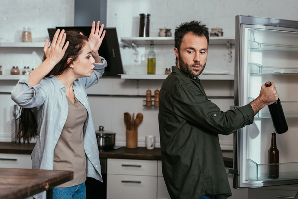 Woman quarreling while husband taking wine bottle from fridge - Valokuva, kuva