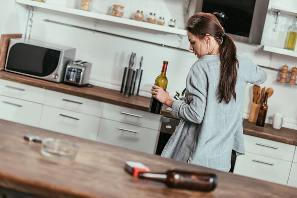 Selectieve focus van vrouw met wijnfles en sigaretten met bier op keukentafel - Foto, afbeelding