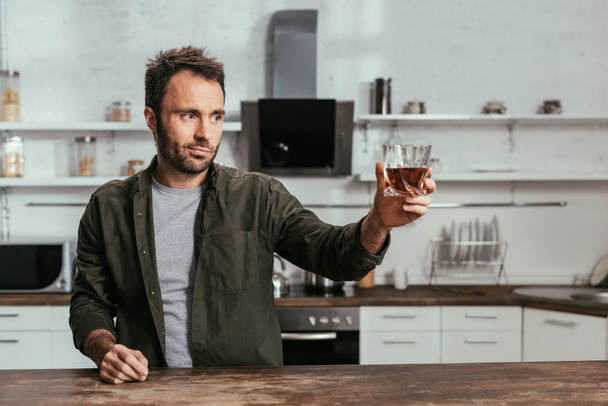 Man with whiskey glass toasting to someone on kitchen - Photo, Image
