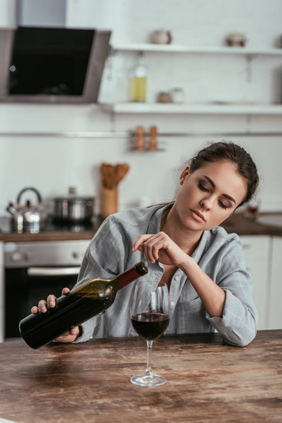 Droevige vrouw met alcohol verslaafde gieten wijn in glas op de keuken - Foto, afbeelding