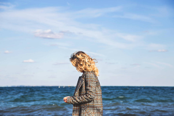 Όμορφη κοπέλα περπατά το φθινόπωρο και εξασκεί τη σκέψη δίπλα στη θάλασσα. - Φωτογραφία, εικόνα