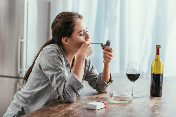 Woman smoking cigarette with wine on kitchen table - Фото, зображення