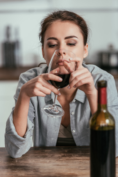 Selektiver Fokus einer traurigen Frau, die auf ein Weinglas blickt - Foto, Bild