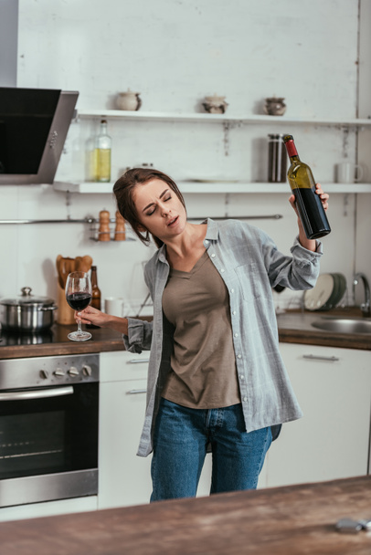 Žena s alkoholem závisela na držení sklenice a láhve vína v kuchyni - Fotografie, Obrázek