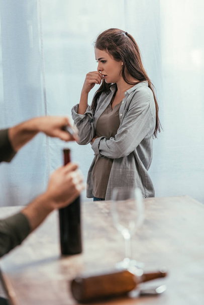 Selective focus of worried woman and man opening wine bottle at home - Φωτογραφία, εικόνα