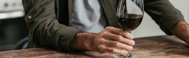 Обрезанный вид человека, держащего бокал вина за столом, панорамный снимок
 - Фото, изображение