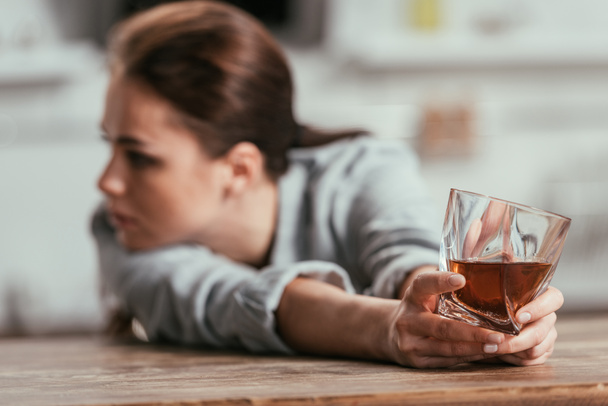 Selective focus of sad woman holding whiskey glass at table - Фото, зображення