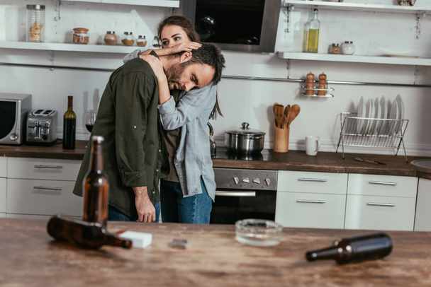 Enfoque selectivo de la mujer calmando marido preocupado con la adicción al alcohol en la cocina
 - Foto, Imagen