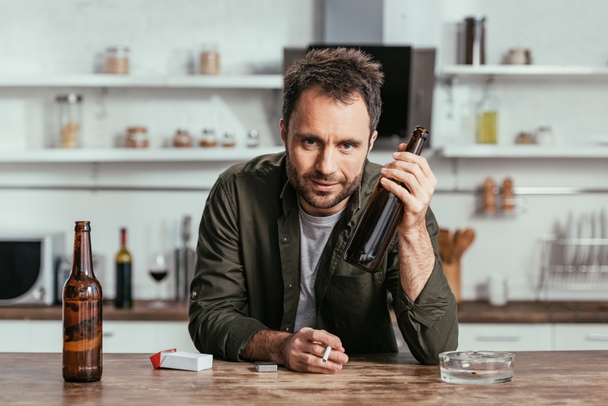 Alcohol addicted man with cigarette holding beer bottle and looking at camera - Foto, Bild