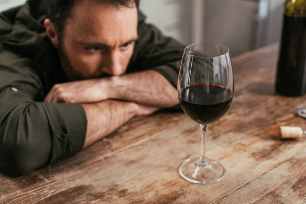 Selective focus of pensive man looking at wine glass on table - 写真・画像