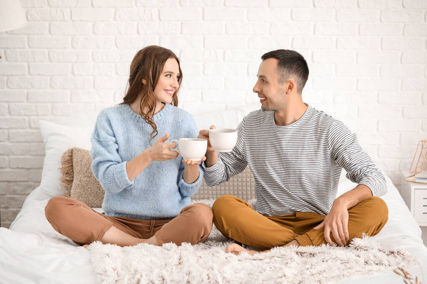 Beautiful young couple drinking tea on bed at home - Photo, Image