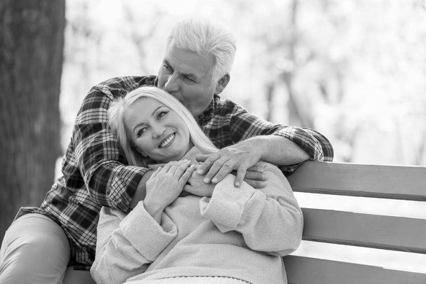 Black and white portrait of loving mature couple sitting on bench in autumn park - Photo, Image