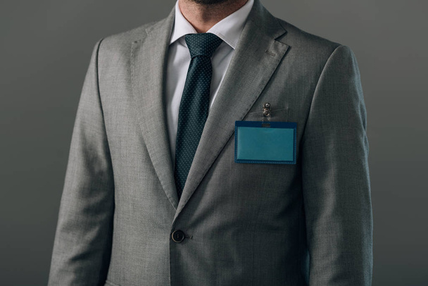 Cropped view of man in suit with badge isolated on grey - Fotografie, Obrázek
