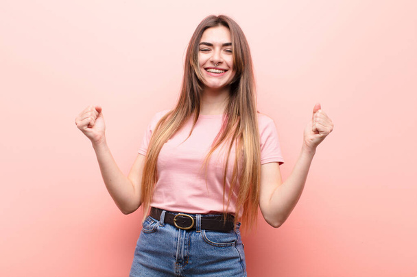 young pretty woman looking extremely happy and surprised, celebrating success, shouting and jumping against pink wall - Photo, Image
