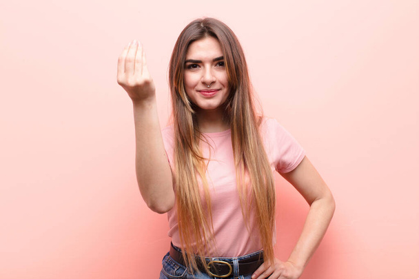 молодая красивая женщина делает капис или денежный жест, приказывая тебе оплатить свои долги! против розовой стены - Фото, изображение