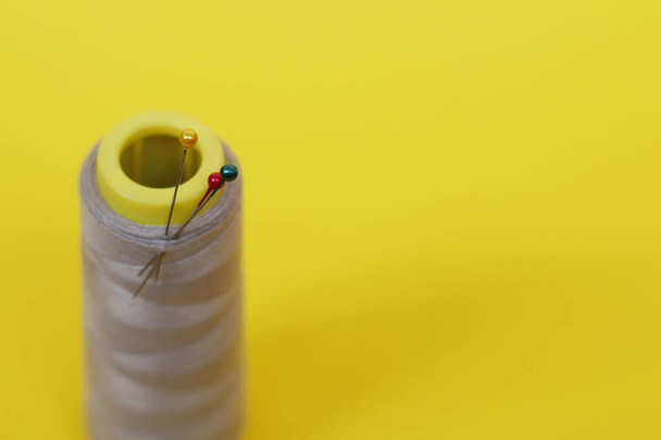 One large spool of thread and needle on a yellow background. - Fotografie, Obrázek