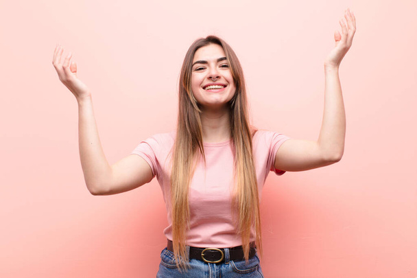 young pretty woman feeling happy, amazed, lucky and surprised, celebrating victory with both hands up in the air against pink wall - Zdjęcie, obraz