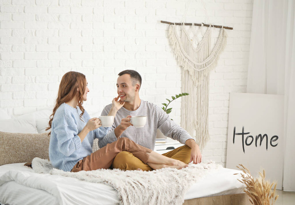 Beautiful young couple drinking tea on bed at home - Photo, Image