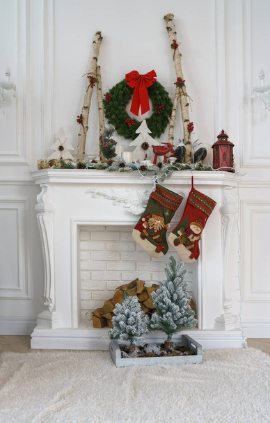 Chimenea blanca decorada para Navidad con pequeños árboles de Navidad y calcetines rojos par
 - Foto, imagen