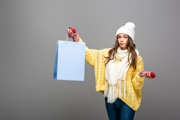 sad woman in winter outfit with shopping bag on grey background - Foto, immagini
