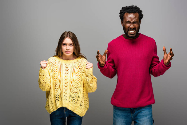 pareja interracial enojado en suéteres de punto sobre fondo gris
 - Foto, Imagen