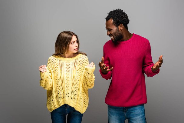 en colère couple interracial en chandails tricotés se regardant sur fond gris
 - Photo, image
