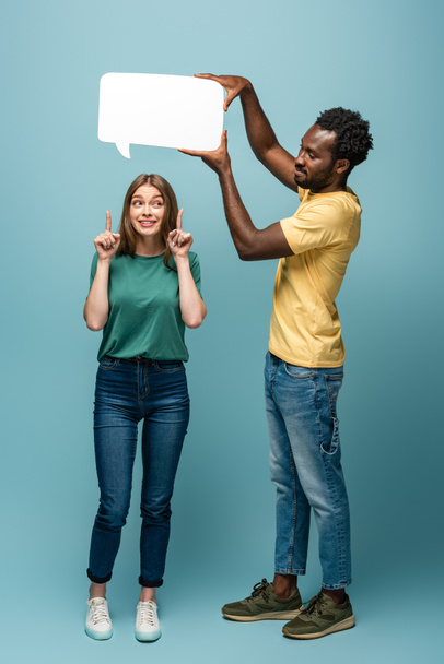 Afrikanisch-amerikanischer Mann hält Sprechblase über Freundin und zeigt Idee Geste auf blauem Hintergrund - Foto, Bild