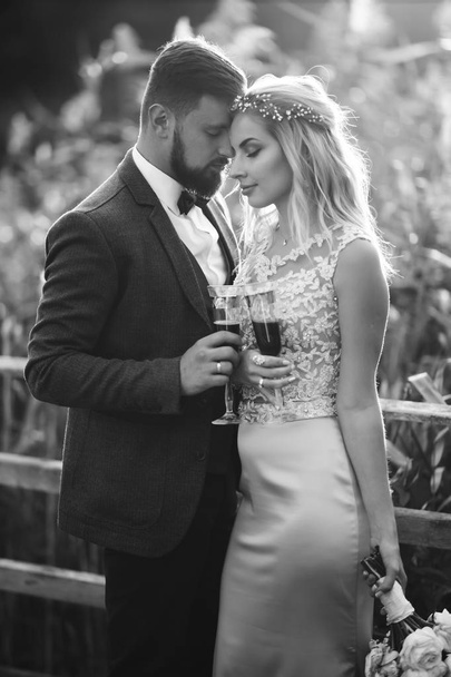 Black and white foto stylish couple of newlyweds posing on a bridge on wedding day. Handsome bearded groom admires and kisses pretty bride. Together. The concept of youth, love, fashion and lifestyle. - Φωτογραφία, εικόνα