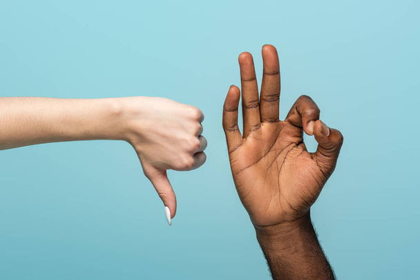 cropped view of interracial couple showing thumb down and okay sign isolated on blue - Valokuva, kuva
