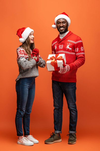 Afrikanisch-amerikanischer Mann verschenkt Weihnachtsgeschenk an glückliche Freundin auf orangefarbenem Hintergrund - Foto, Bild