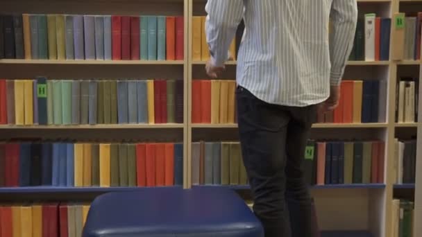 der Kerl sucht sich ein Buch im Regal einer Buchhandlung aus - Filmmaterial, Video