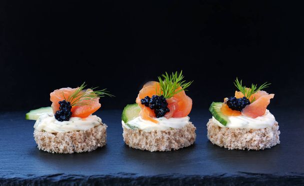 Canapés elegantes con salmón ahumado y caviar negro en empanadas de grano entero sobre bandeja de pizarra negra
 - Foto, imagen