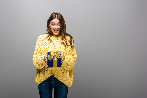 excited happy woman in yellow sweater holding gift box on grey background - 写真・画像