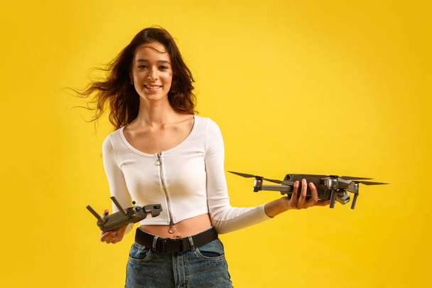 Teen girl launches aerial drone quadcopter. Isolated on a yellow background. Aerial photography. - Foto, imagen