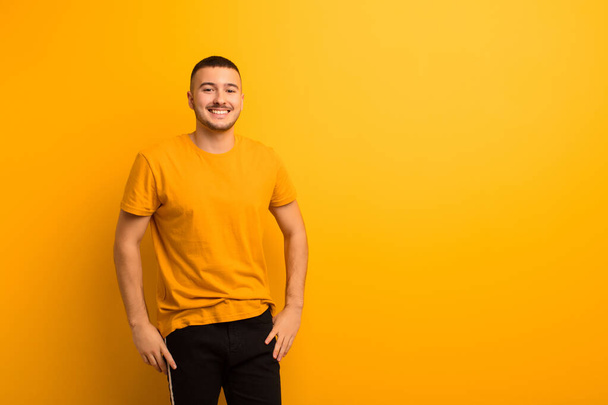 young handsome man looking happy and goofy with a broad, fun, loony smile and eyes wide open against flat background - Foto, imagen