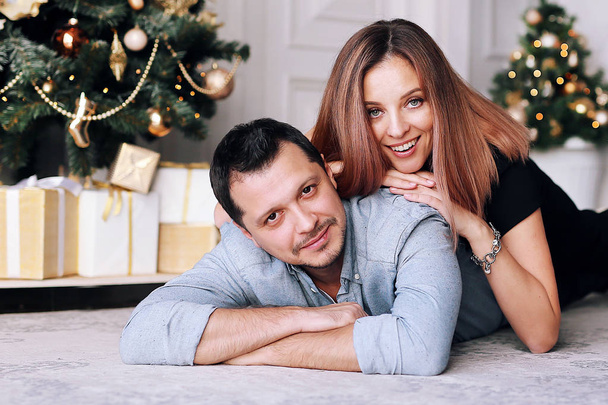 Beautiful young couple next to the Christmas tree. A young woman and a man are smiling and having fun together. - Foto, Bild