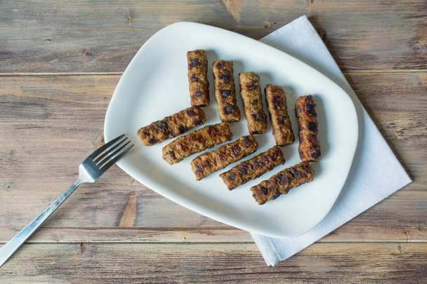 Balkan cuisine. Cevapi - grilled dish of minced meat - on white plate.  Rustic background, flat lay, free space for text  - Photo, Image