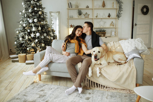 happy couple is sitting near the bed with a dog, christmas. new year at home. family and date - Fotó, kép